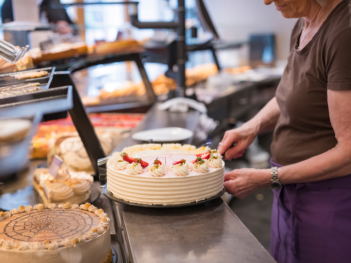 Mitarbeiterin verziert eine Sahnetorte hinter der Vitrine mit frischen Erdbeeren